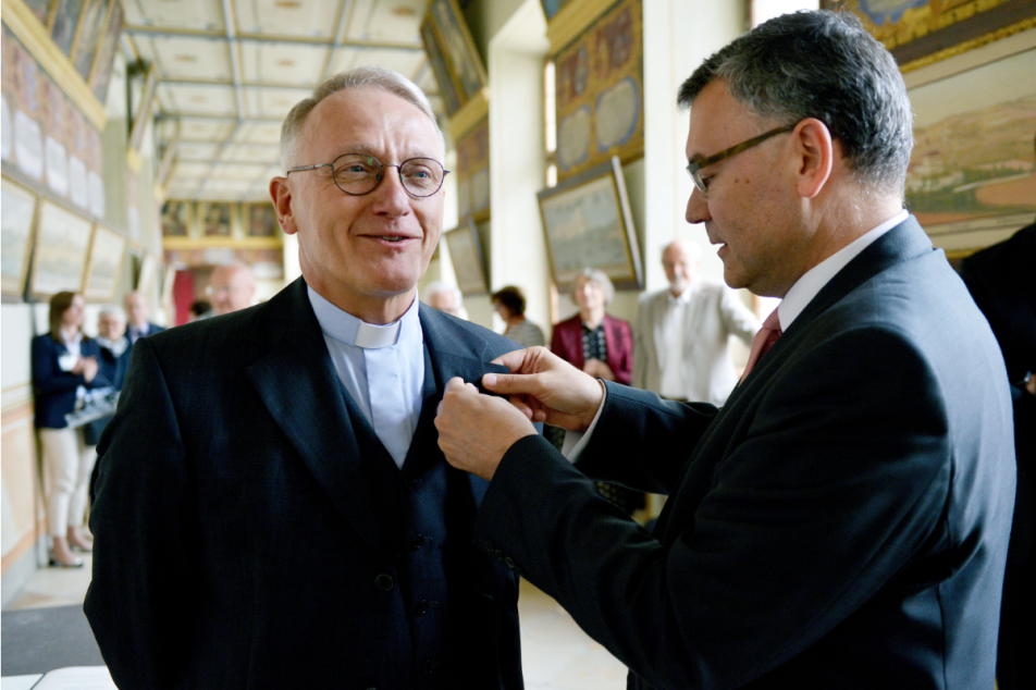 Prof. Dr. Marc-Aeilko Aris wird von Staatsminister Dr. Florian Herrmann das Verdienstkreuz am Revers befestigt.